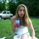 A cute girl with blonde hair is sitting in the grass eating when all of a sudden she blows a stinky, silent fart. The fart makes her get out of there, and proceeds to act silly for the rest of the video clip.